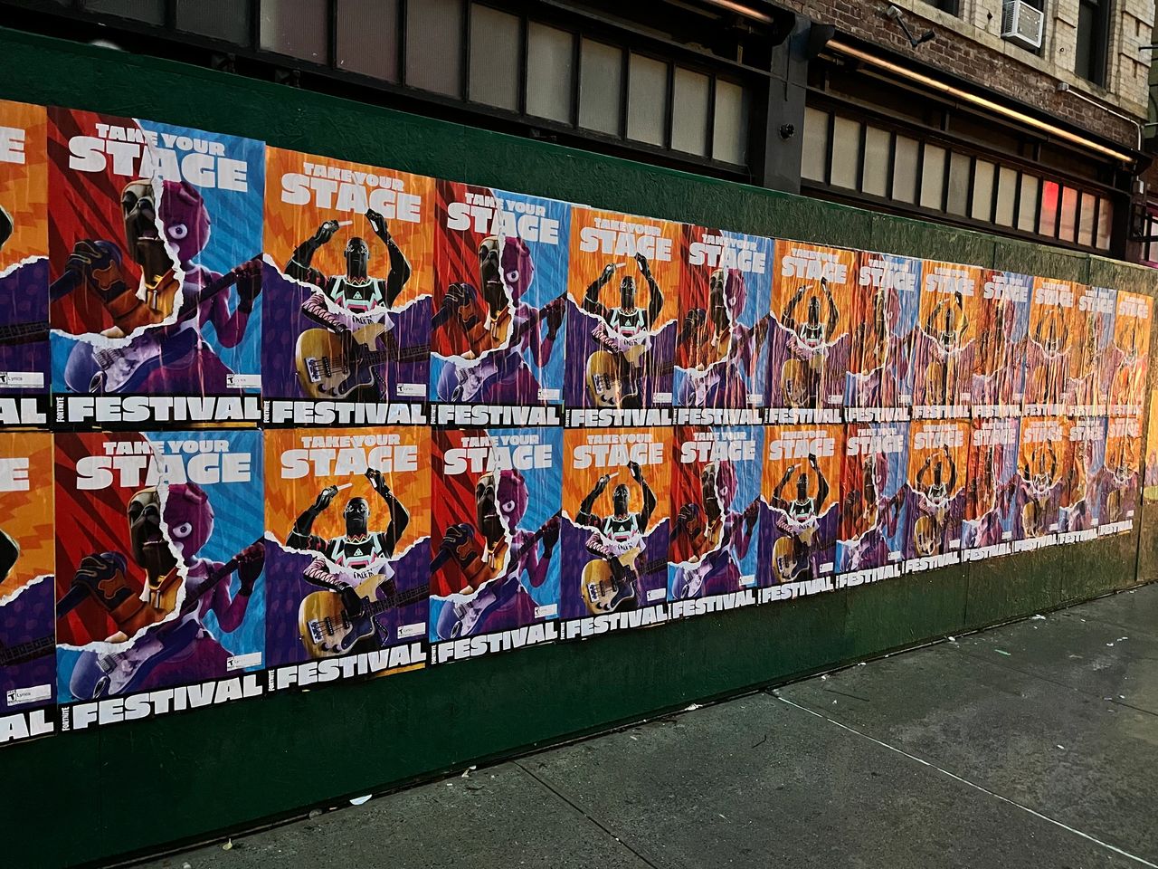Wheatpaste posters promoting a festival, featuring vibrant graphics of musicians and the text "Take Your Stage," displayed on a wall in an urban setting.