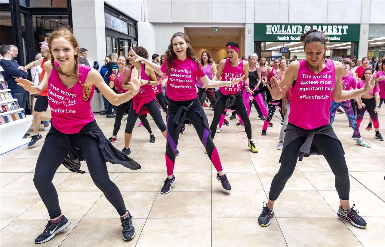 Group of dancers in vibrant pink shirts performing a flash mob in a public space, promoting a race event, showcasing the energy and unity of guerrilla marketing through music and dance.