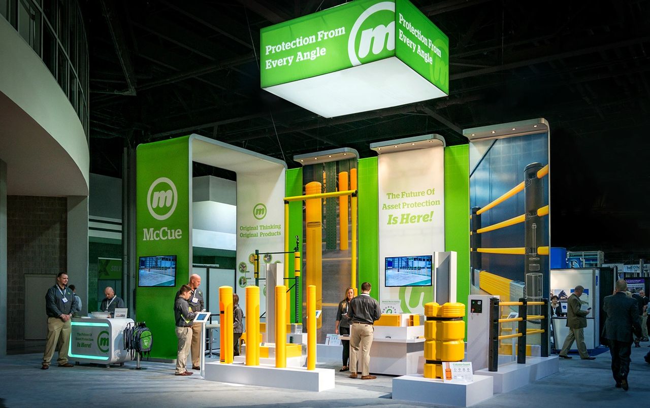 Trade show booth for McCue showcasing asset protection solutions, featuring bright yellow safety products and promotional signage emphasizing "Protection From Every Angle."