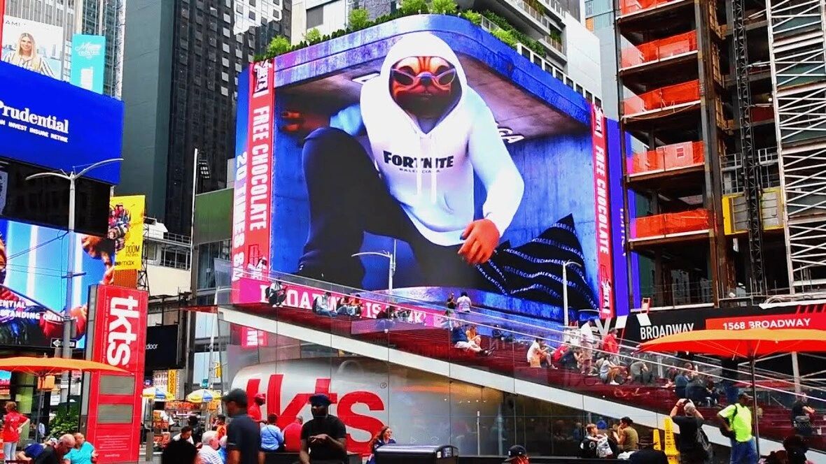 Digital billboard featuring a vibrant animated character wearing a Fortnite hoodie, showcasing augmented reality advertising in a bustling urban setting, surrounded by people and other advertisements.