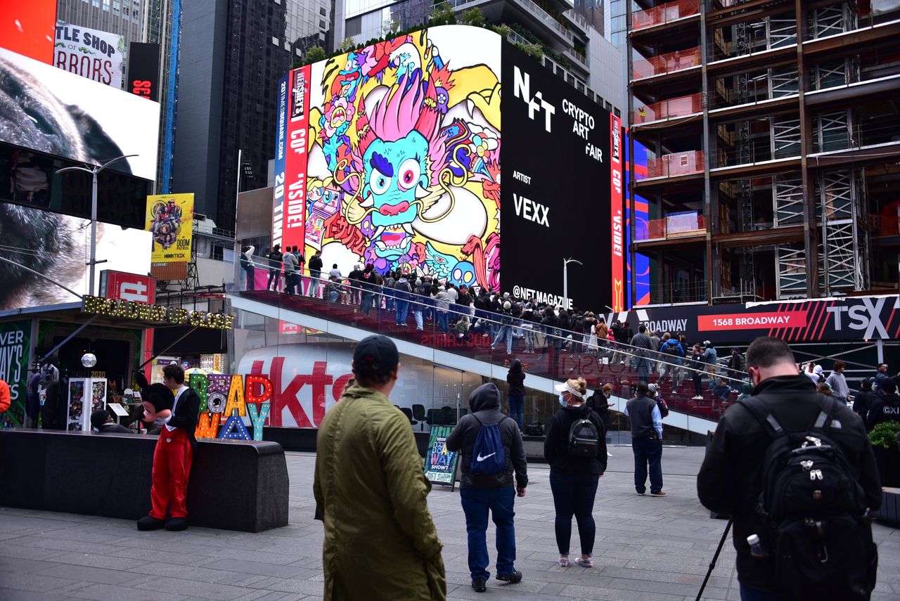 Billboard in Times Square featuring colorful NFT art by artist Vexx, attracting crowds and showcasing vibrant advertisements.