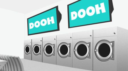 Laundromat interior featuring modern washing machines and digital advertising screens displaying "DOOH," emphasizing digital marketing strategies for attracting customers.