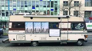 Vintage camper van displaying movie advertising, showcasing guerrilla marketing tactics for independent films in urban setting.