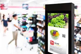 Digital point of sale advertising display featuring a salad promotion with vibrant greens and pricing, enhancing brand visibility and influencing customer purchasing decisions in a grocery store setting.
