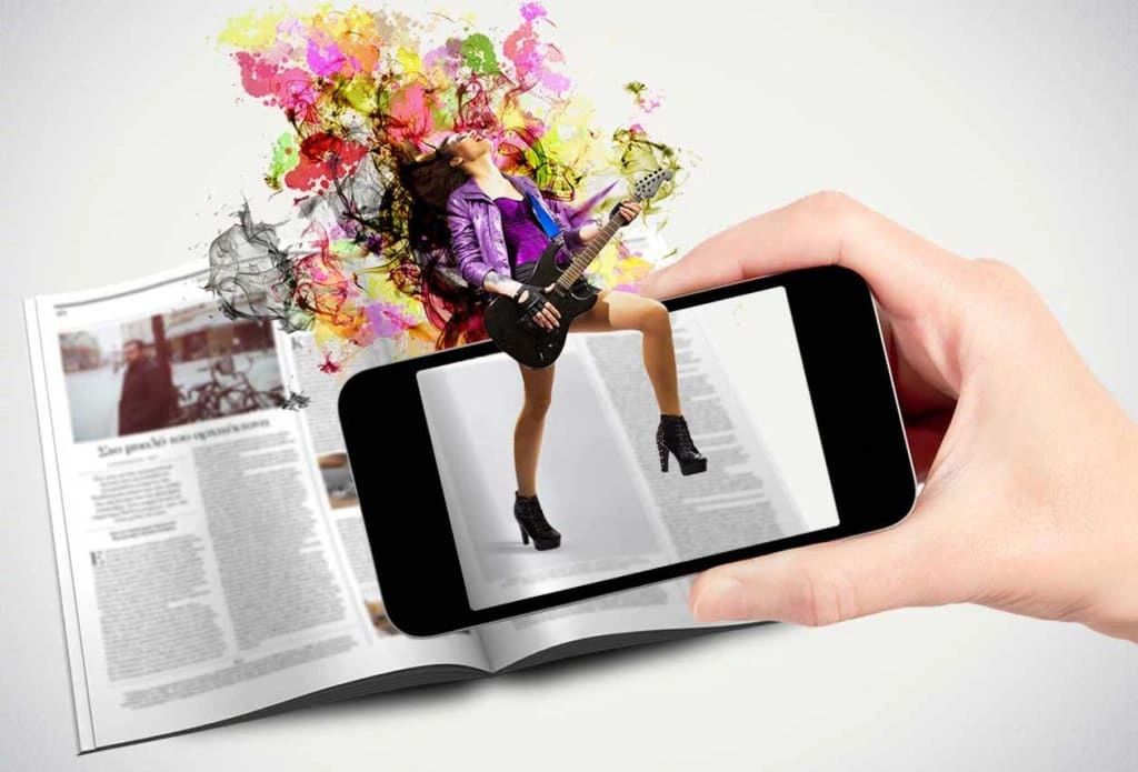 Hand holding smartphone displaying augmented reality image of a woman playing guitar, surrounded by colorful splashes, overlaid on an open magazine, illustrating interactive marketing and consumer engagement.