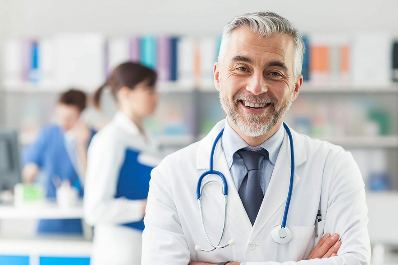 The importance of doctor office advertising cannot be underestimated. Smiling male doctor in a white coat with a stethoscope, showcasing a welcoming healthcare environment, emphasizing trust and patient engagement in digital advertising strategies.