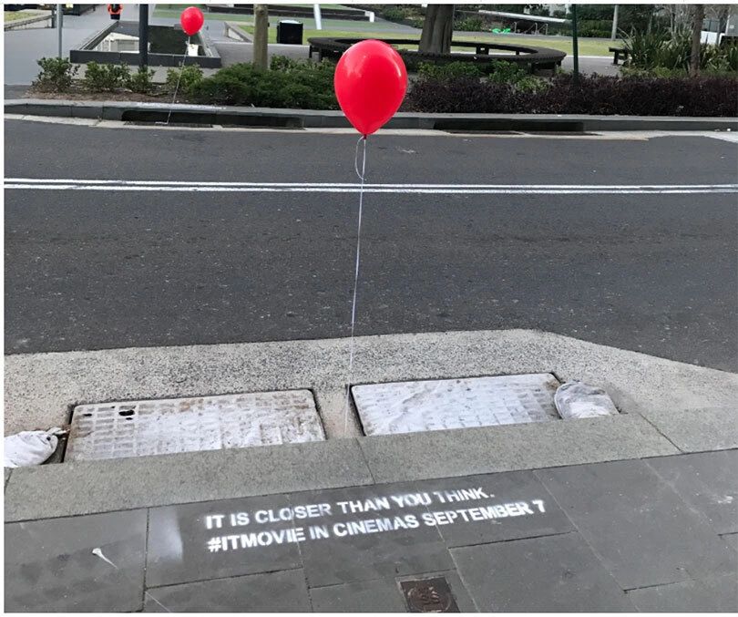 it Campaign Red balloon tied to a street curb with spray-painted text reading "IT IS CLOSER THAN YOU THINK. #ITMOVIE IN CINEMAS SEPTEMBER 7," exemplifying ambient marketing strategy.