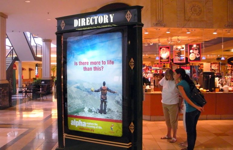 In today's competitive market, enhancing brand awareness is crucial for driving business growth. Directory display in mall featuring an advertisement with the question "Is there more to life than this?" and a scenic mountain background, with two women engaging with the display.
