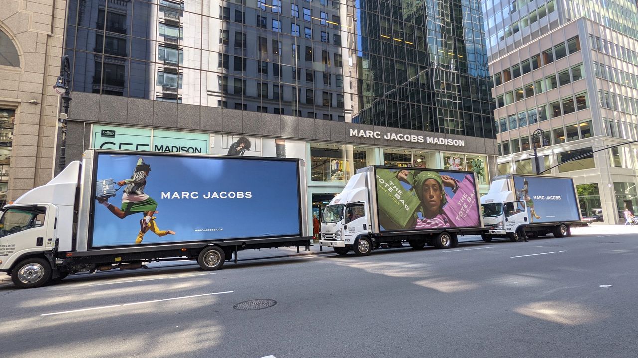 Marc Jacobs Madison storefront with three trucks displaying vibrant fashion advertisements featuring bold imagery and branding, highlighting innovative marketing strategies in the fashion industry.