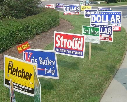 Political yard signs displaying candidates' names and positions, featuring bright colors for visibility, promoting local elections and civic engagement.