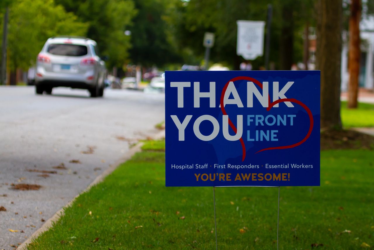 Thank you yard sign for front line workers, featuring bold text and a heart design, positioned on a grassy area near a road, emphasizing community appreciation in local marketing.
