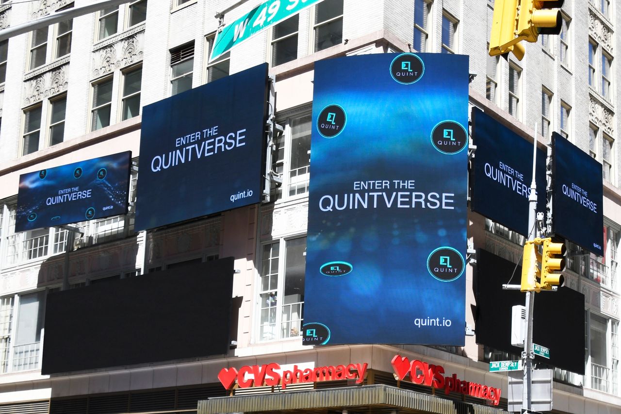 Times Square billboard advertising featuring multiple screens displaying "Enter the Quintverse" and the website "quint.io," with a CVS pharmacy visible below.