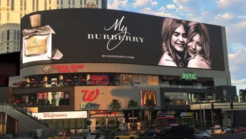 Billboard advertisement for Burberry featuring two women smiling, promoting the fragrance "My Burberry," located in a busy Las Vegas commercial area.