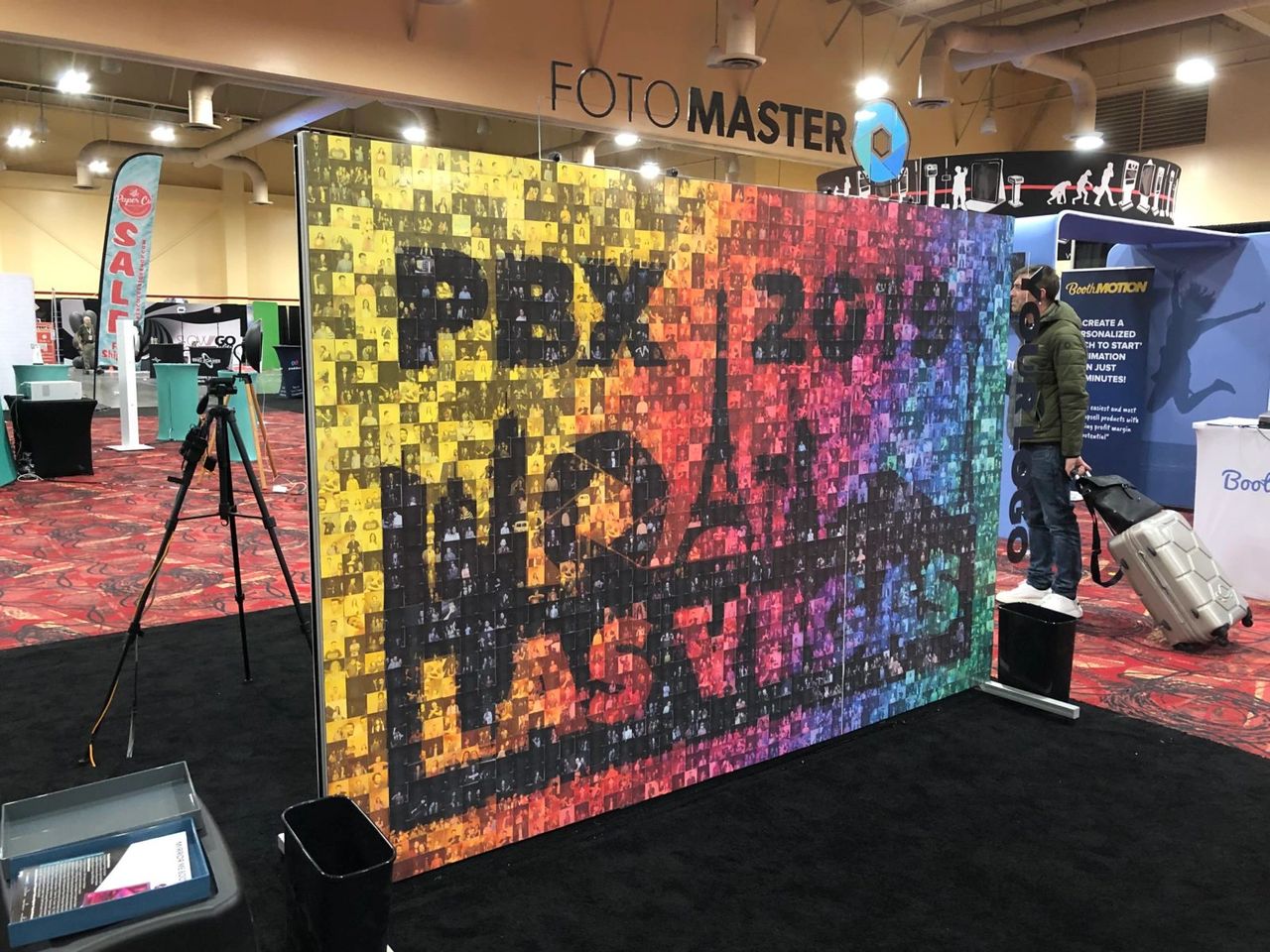 Trade show booth featuring a colorful photo wall with "PBX 2019" text, surrounded by interactive displays and a participant engaging with the setup, emphasizing innovative marketing strategies and interactive experiences.