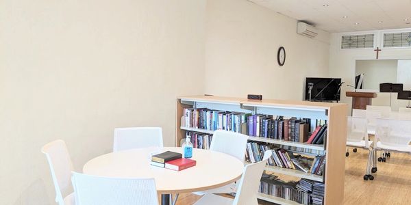 A bright room with a round table, white chairs, and a bookshelf filled with books.