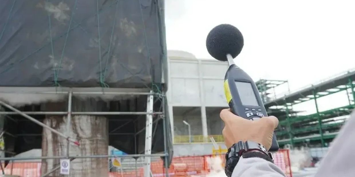 Person holding a sound level meter at a construction site.