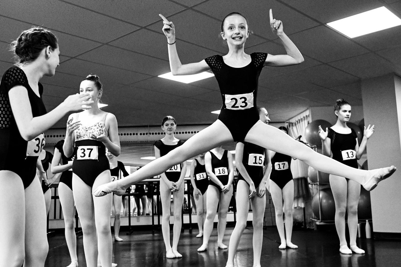 Young ballet dancers in a studio, one mid-leap with a joyful expression.