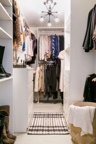 Well-organized walk-in closet with clothes, boots, and a modern light fixture.
