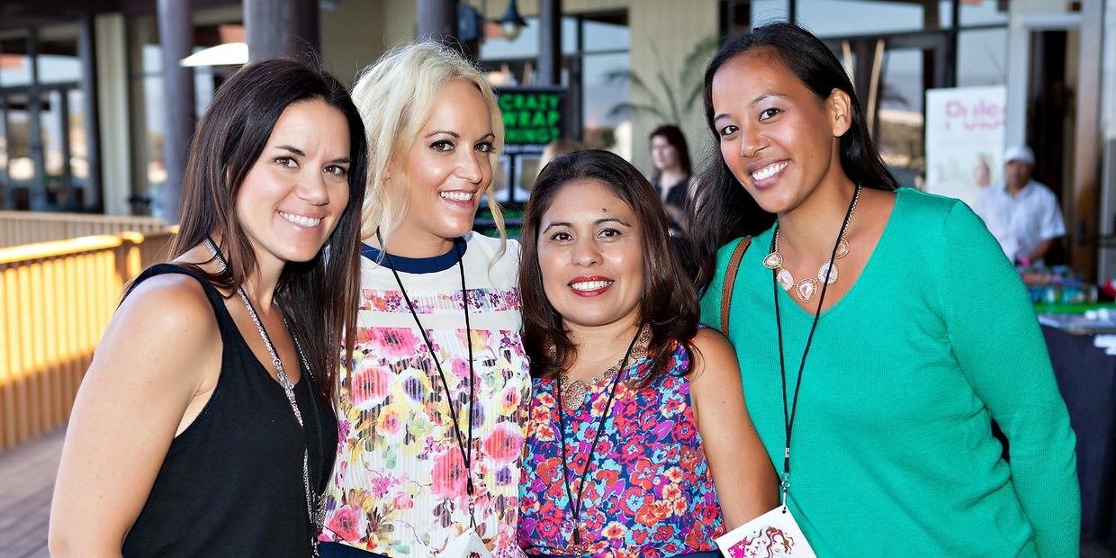 Four smiling women posing together at a social event.