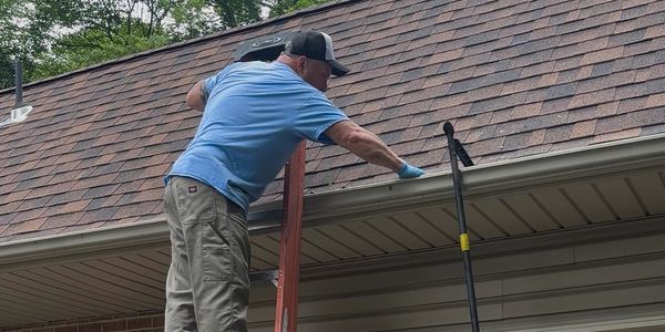 Man on ladder cleaning gutters of a house.