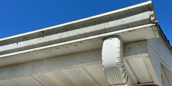 Close-up of a white gutter and downspout on a house under a clear blue sky.