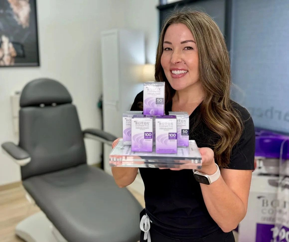 Smiling woman holding Botox Cosmetic product boxes in a clinic room.