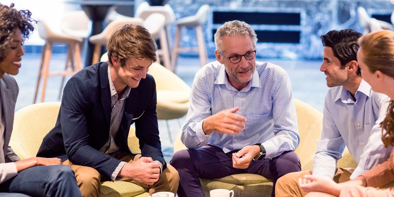 Group of professionals having a friendly discussion over coffee in a modern office lounge.