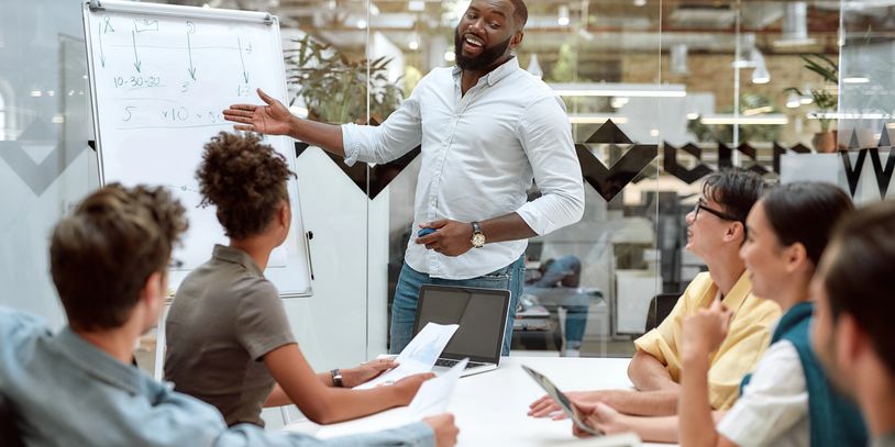 A man presents ideas on a whiteboard to an engaged team in a modern office.