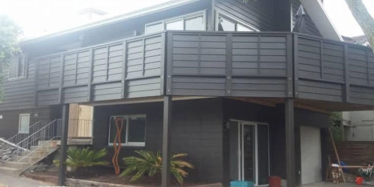 Two-story dark gray house with large balcony.