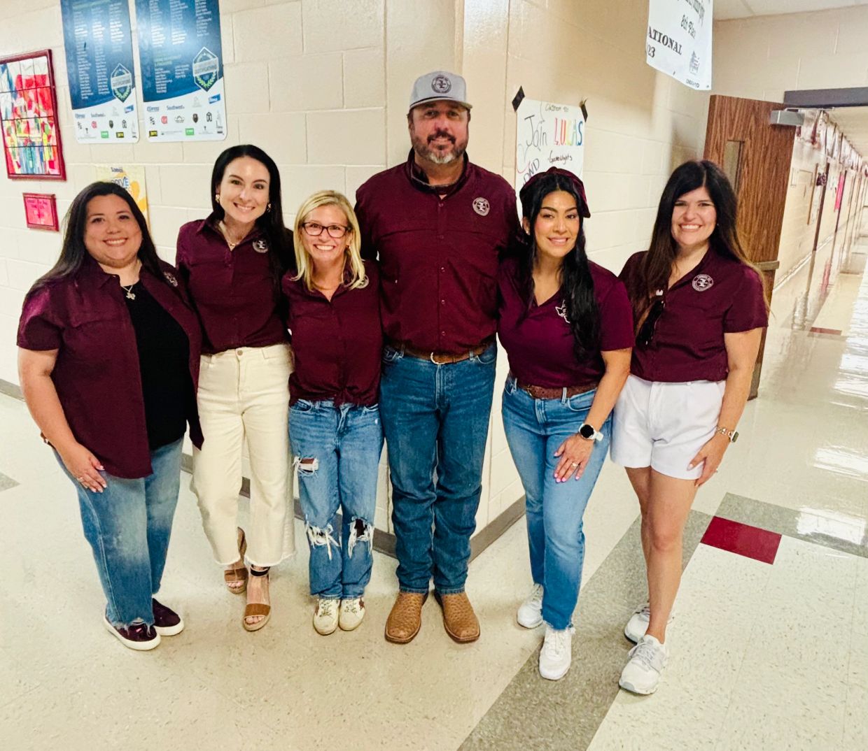 Group of six adults posing in a hallway wearing matching maroon shirts.