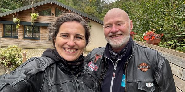 Two smiling people in leather jackets taking a selfie outdoors.