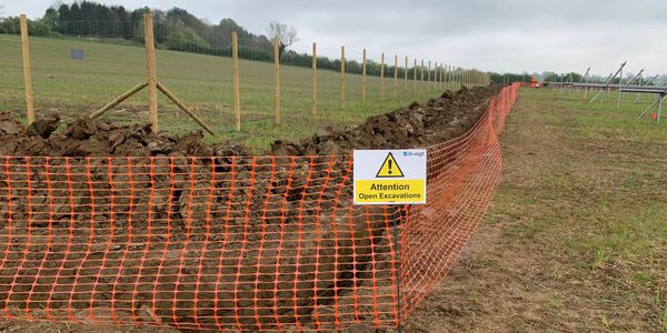 Orange safety fence around a long open trench with a warning sign.