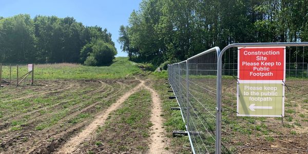 Construction site with signs directing to the public footpath beside a dirt trail.