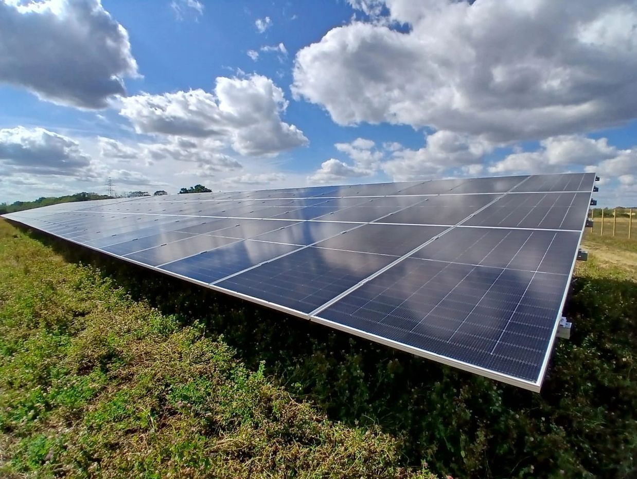 Solar panels under a partly cloudy sky in a green field.