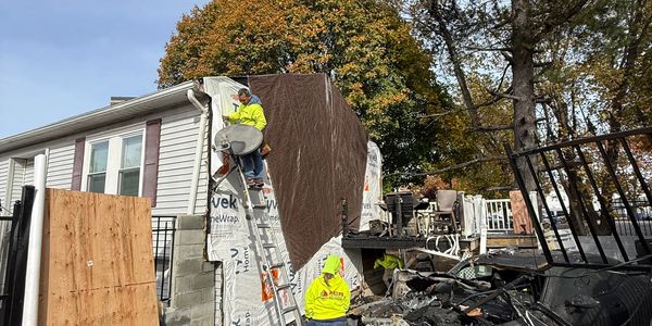 Workers repairing a house exterior with a ladder and tarp.