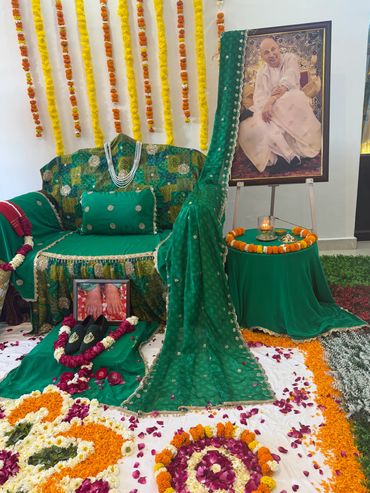A memorial setup with a green saree, flowers, and a framed photograph.