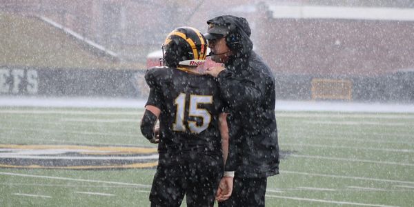 Football coach advises player during snowy game.