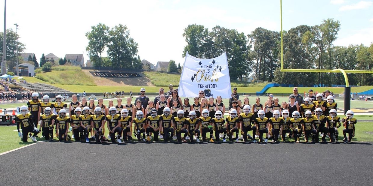 Youth football team posing on field with a banner reading 'This is Chiefs Territory'.