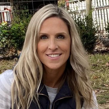 Smiling woman with blonde hair outdoors in casual fall clothing.