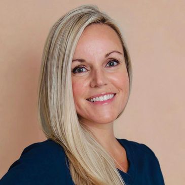 Smiling woman with blonde hair in navy blue scrubs poses confidently.