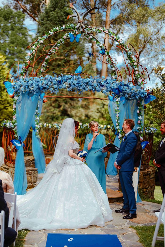 Outdoor wedding ceremony with blue and white floral decorations and butterflies.