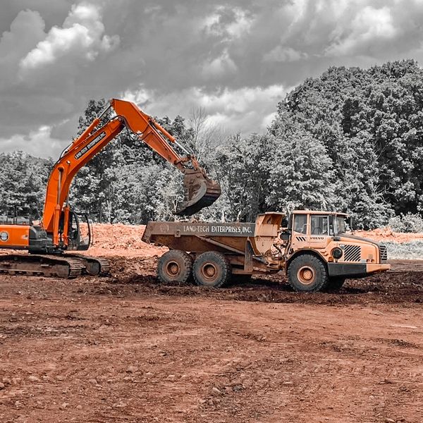 Orange excavator loading dirt into a dump truck at a construction site.