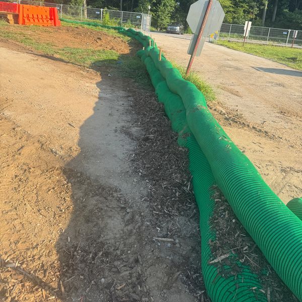 Green erosion control tubes line a dirt path near a stop sign and construction barriers.