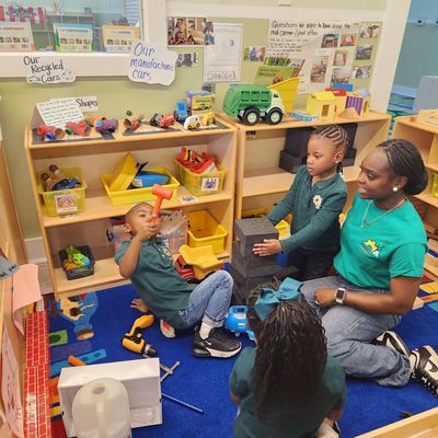 Children and teacher playing with toy trucks and blocks in a classroom.