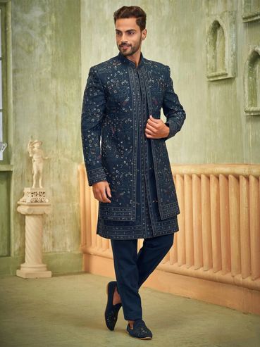 Man in a navy blue embroidered sherwani standing indoors.