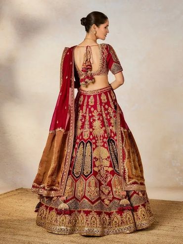 Back view of a woman wearing an intricately embroidered red and gold traditional Indian lehenga.