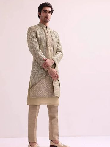 Man wearing a traditional beige embroidered sherwani with churidar pants.