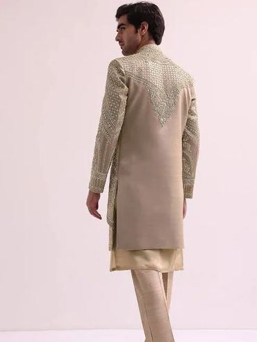 Man wearing an intricately embroidered beige sherwani with matching pants.