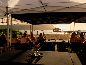 People dining under tents at sunset by the beach.