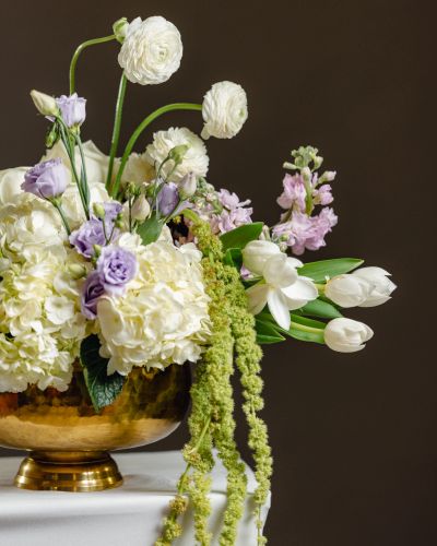 Elegant floral arrangement in a golden vase with white and purple flowers.